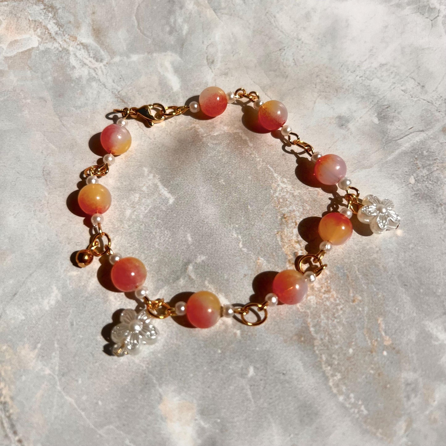 A gold chain bracelet with pink and white beads and two small flower charms